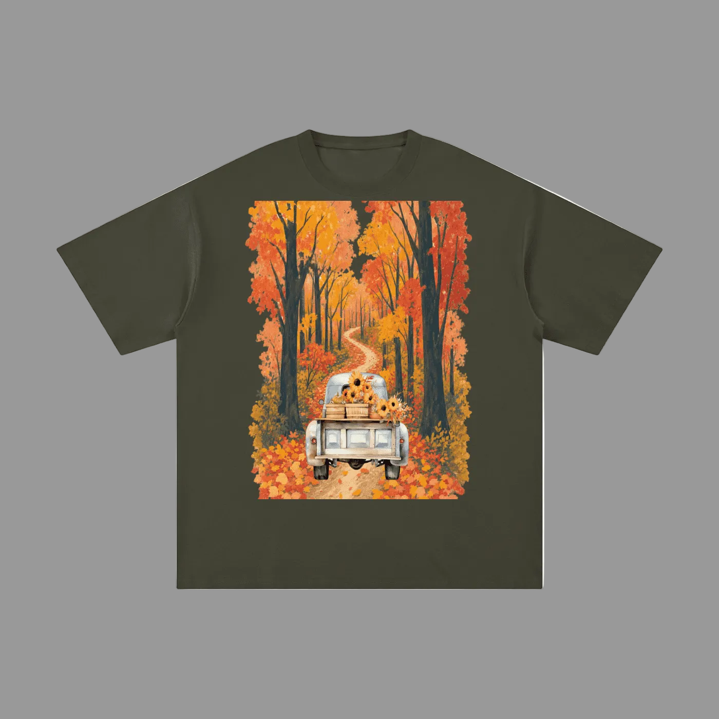 An olive green short-sleeve t-shirt with a large rectangular graphic print on the front. The graphic shows a white pickup truck driving down a winding road lined with orange and yellow autumn trees, with sunflowers in the back of the truck.