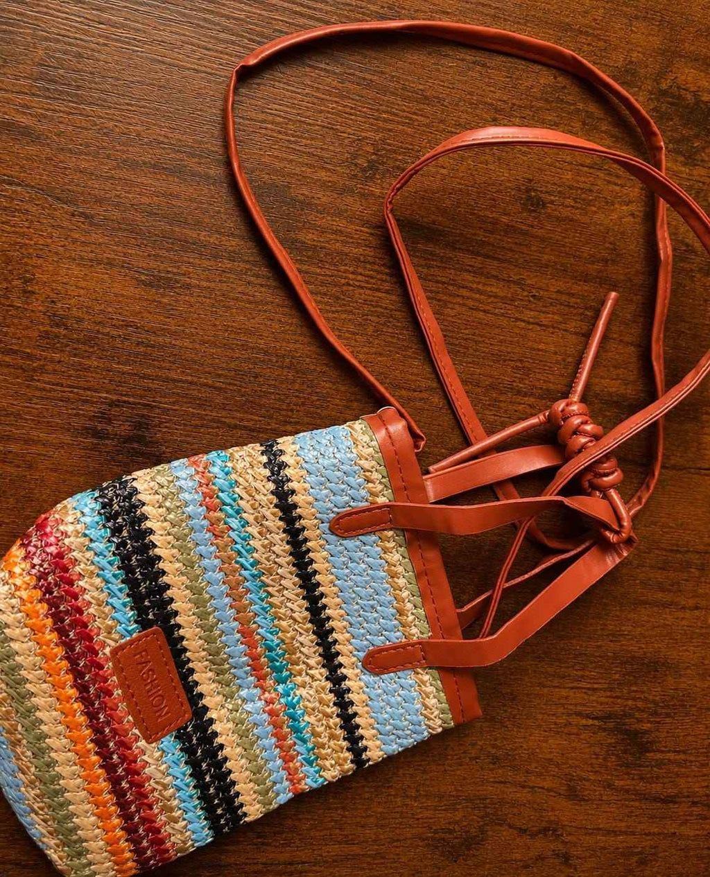Close-up of colorful straw woven crossbody bag with leather straps and adjustable cord