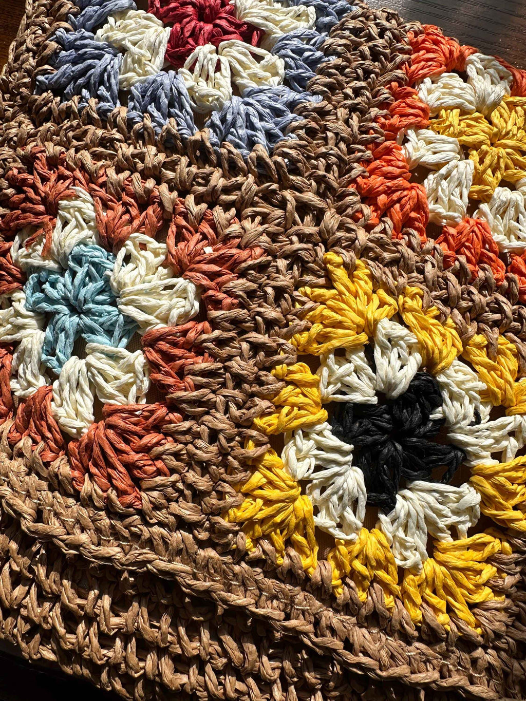 Close-up of handmade granny square crochet pattern with colorful floral motifs and textured yarn stitching