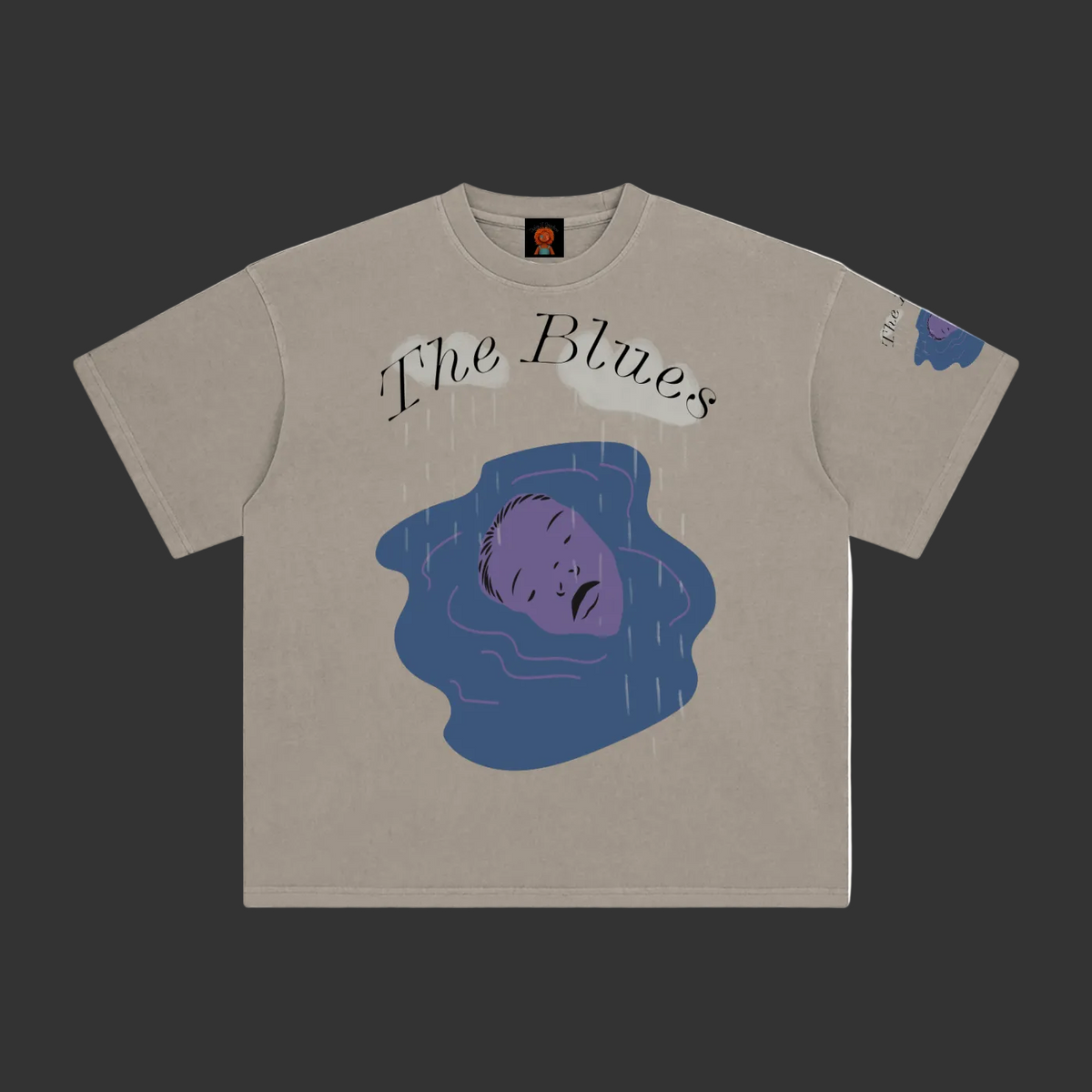 A beige crewneck t-shirt featuring a graphic print of a purple face in blue water with the text 'The Blues' written above, displayed flat against a gray background.