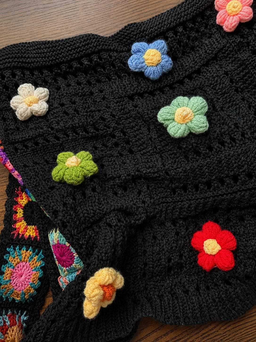 Close-up of handmade crochet tote bag featuring colorful floral appliqués, textured black crochet stitching, and artisan craftsmanship
