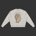 A light beige crewneck sweatshirt featuring a graphic of a side-profile human head with a heart inside the brain, with the words 'Sensation • Energy • Simulation' written above, shown on a plain gray background.