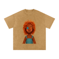 A tan short-sleeve t-shirt with a graphic of a smiling doll character with orange hair and mismatched blue and orange buttons on one eye, displayed on a solid white background.