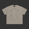 A light gray short-sleeve t-shirt with a black line art graphic of a profile silhouette, a heart, and the text 'We Kind To Your Friend' on the front, displayed flat against a gray background.