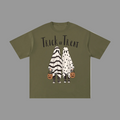 An olive green short-sleeve t-shirt with a 'Trick or Treat' Halloween graphic on the front, featuring two ghost characters in black-and-white and white polka-dot costumes holding jack-o'-lantern buckets, shown on a plain gray background.