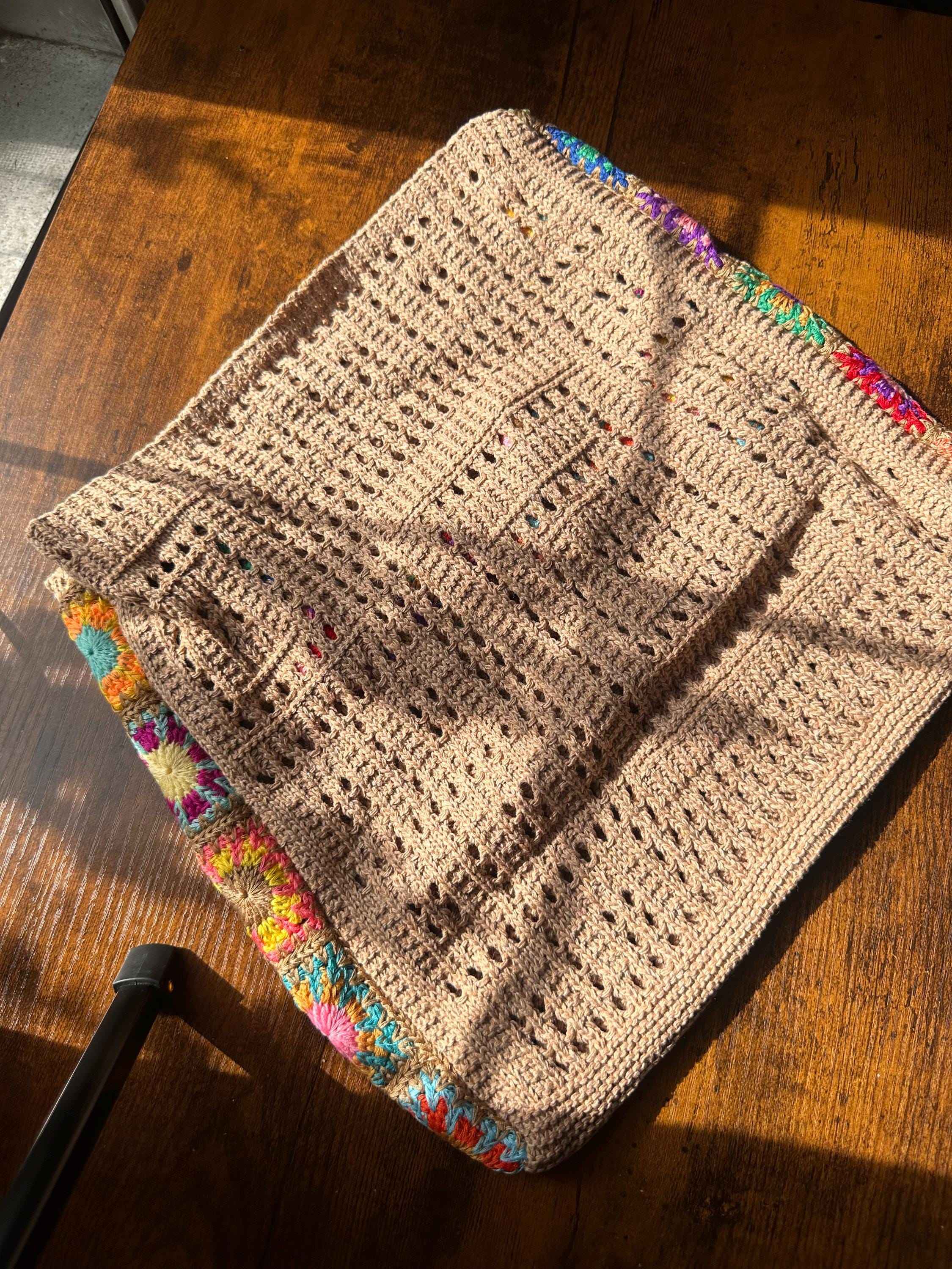 Boho crochet tote bag with colorful granny square border on wooden table