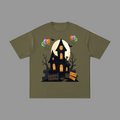 An olive green short-sleeve t-shirt with a graphic of a spooky haunted house, a full moon, jack-o'-lantern balloons, and bare trees on a graybackground.