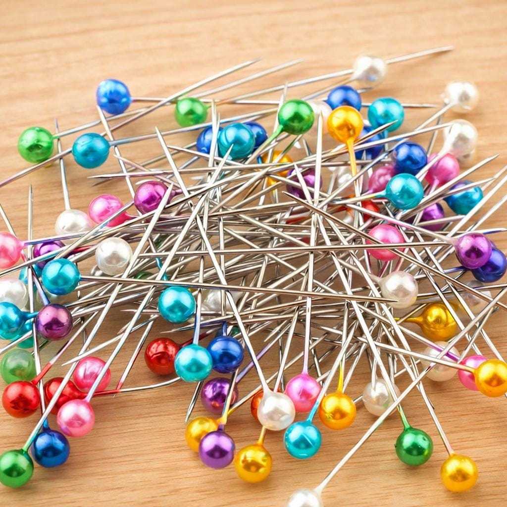 Assorted colorful pearl head sewing pins scattered on a wooden surface for quilting, sewing, and fabric crafting