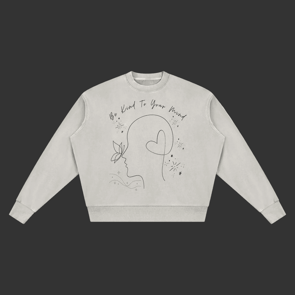 A light gray crewneck sweatshirt with a black line art graphic of a face, butterfly, and heart, accompanied by the text 'Be Kind To Your Mind' on a plain gray background.