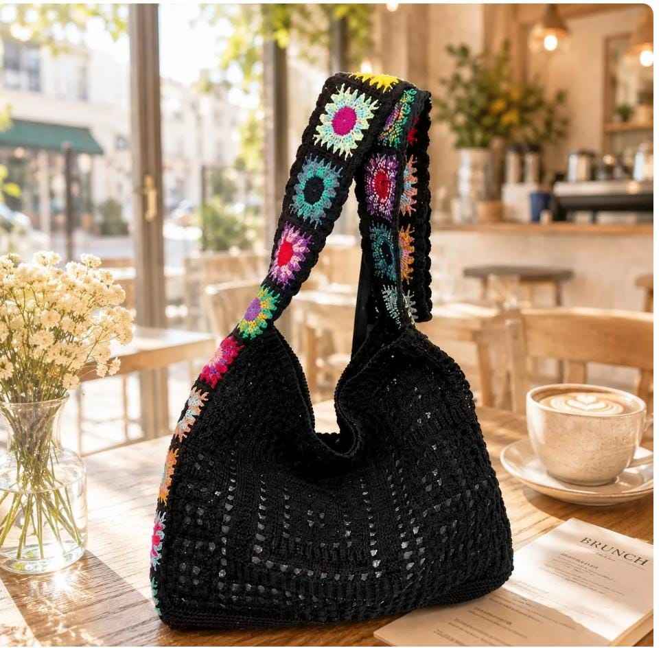 Boho crochet tote bag with colorful granny square strap on wooden table in cafe