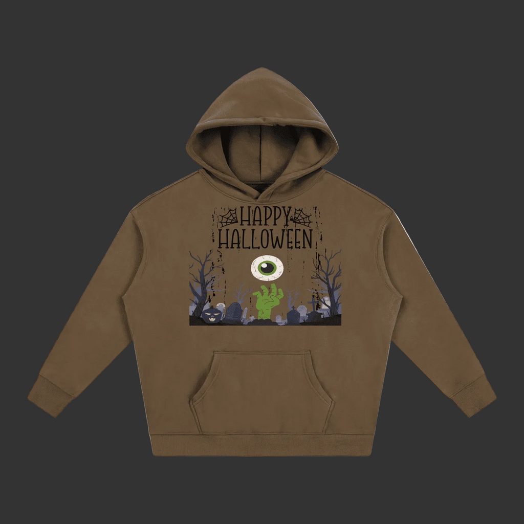 A brown pullover hoodie with a Halloween graphic on the chest, featuring the text 'Happy Halloween' above a spooky scene with a large eye, green hand, and bare trees, shown on a plain grey background.