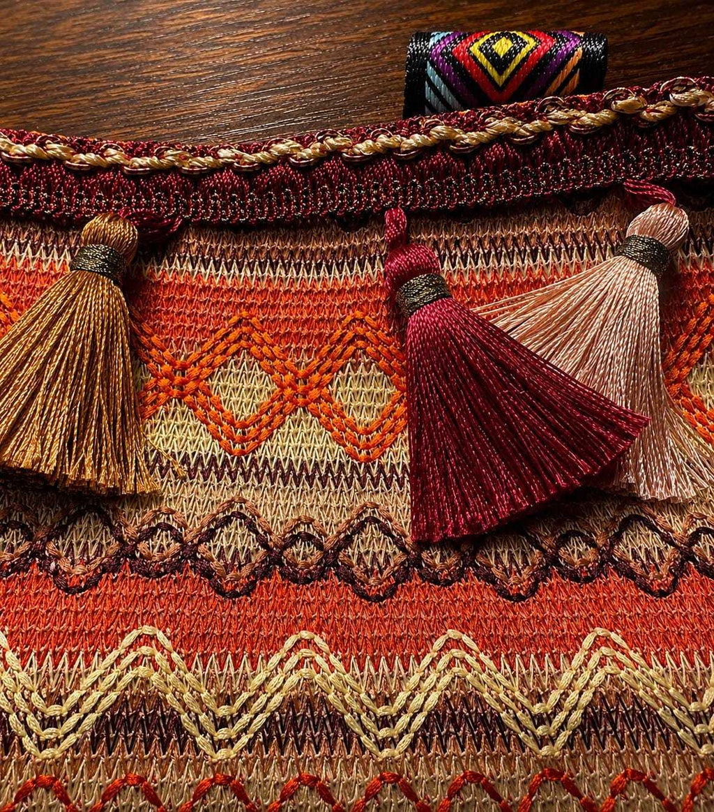 Colorful woven boho handbag with tassels on wooden surface