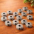 Set of 20 stainless steel sewing machine bobbins arranged on wooden surface for sewing and quilting projects
