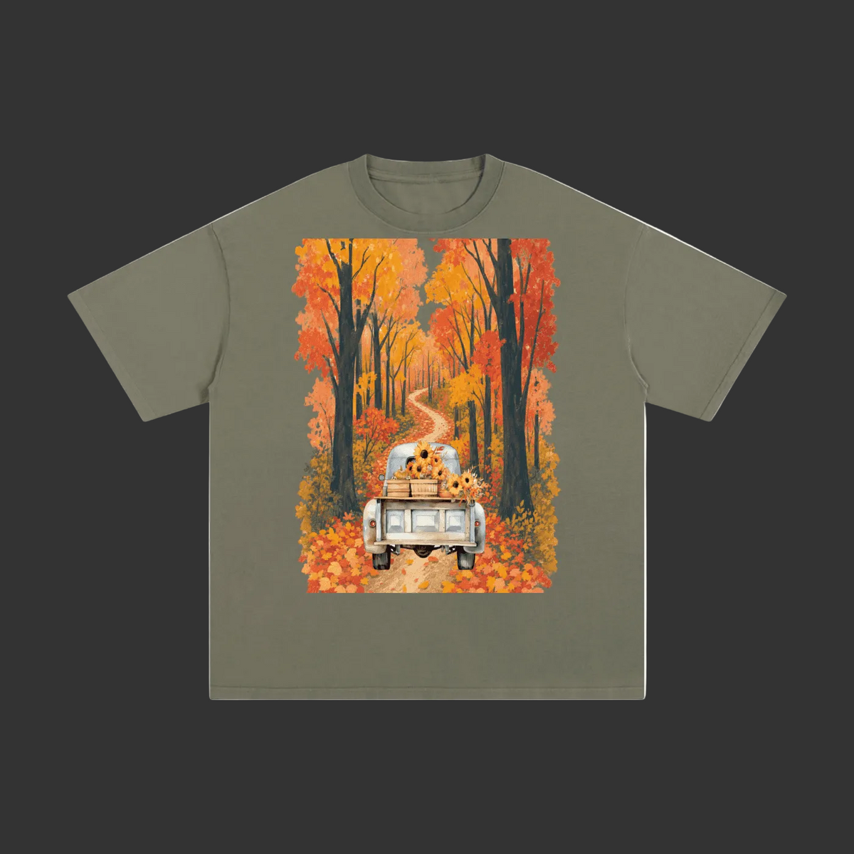 An olive green short-sleeve t-shirt with a large rectangular graphic print on the front. The graphic shows a white pickup truck driving down a winding dirt road lined with orange and yellow autumn trees, with sunflowers sitting in the back of the truck.