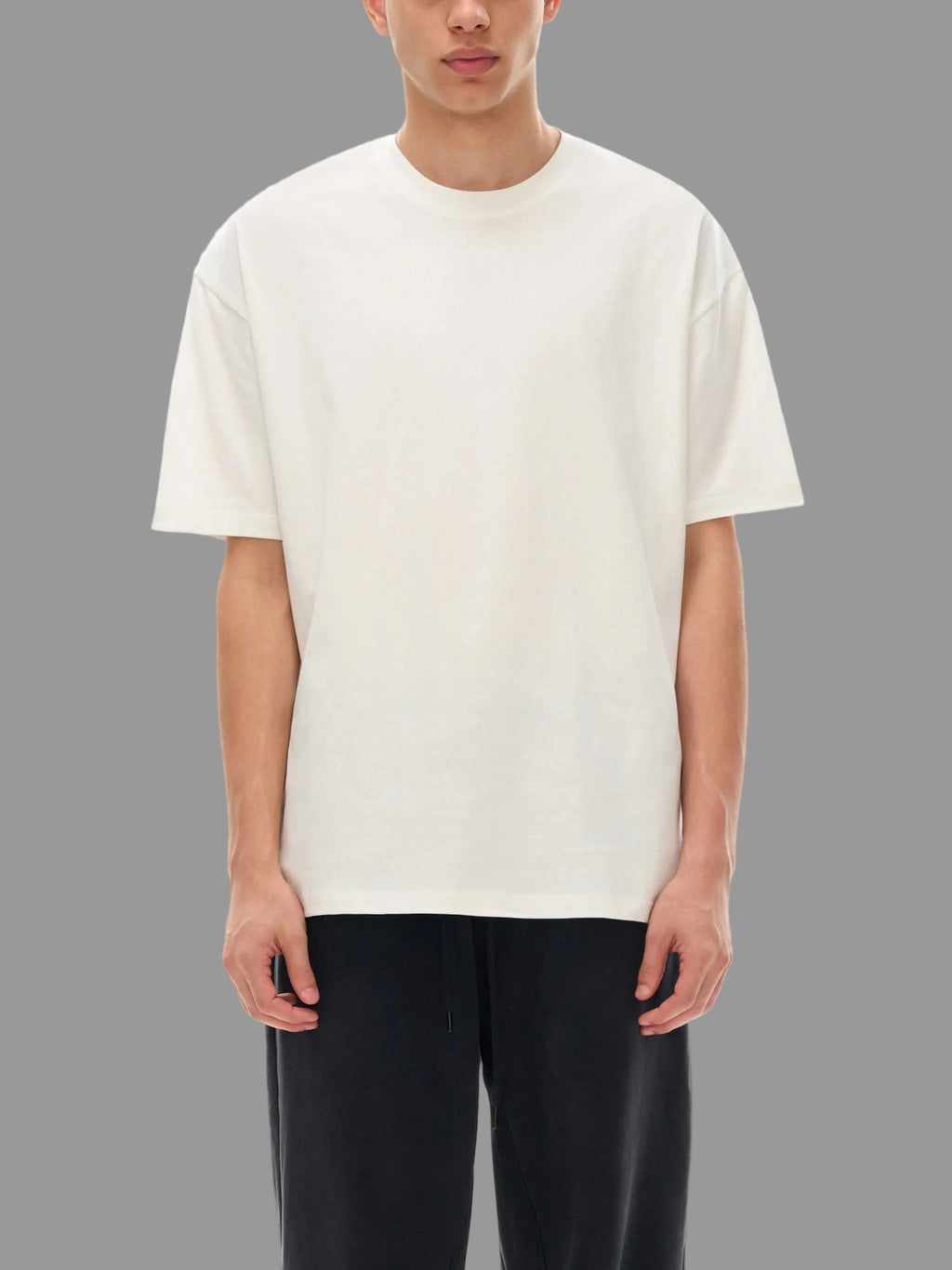 Person wearing a plain white t-shirt and black pants on a gray background