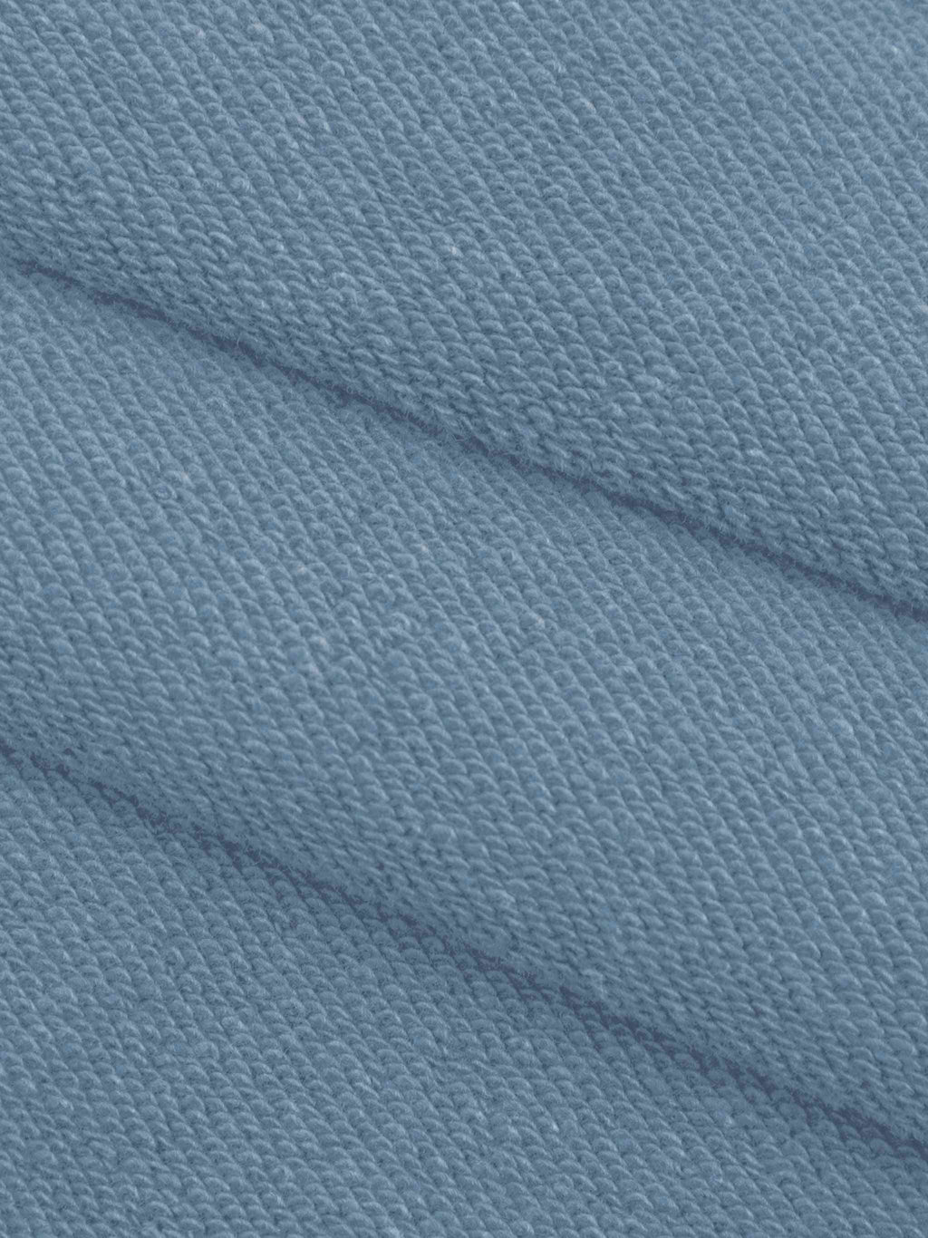 A close-up of textured knit fabric in a dusty light blue color, showing the weave pattern and soft folds.