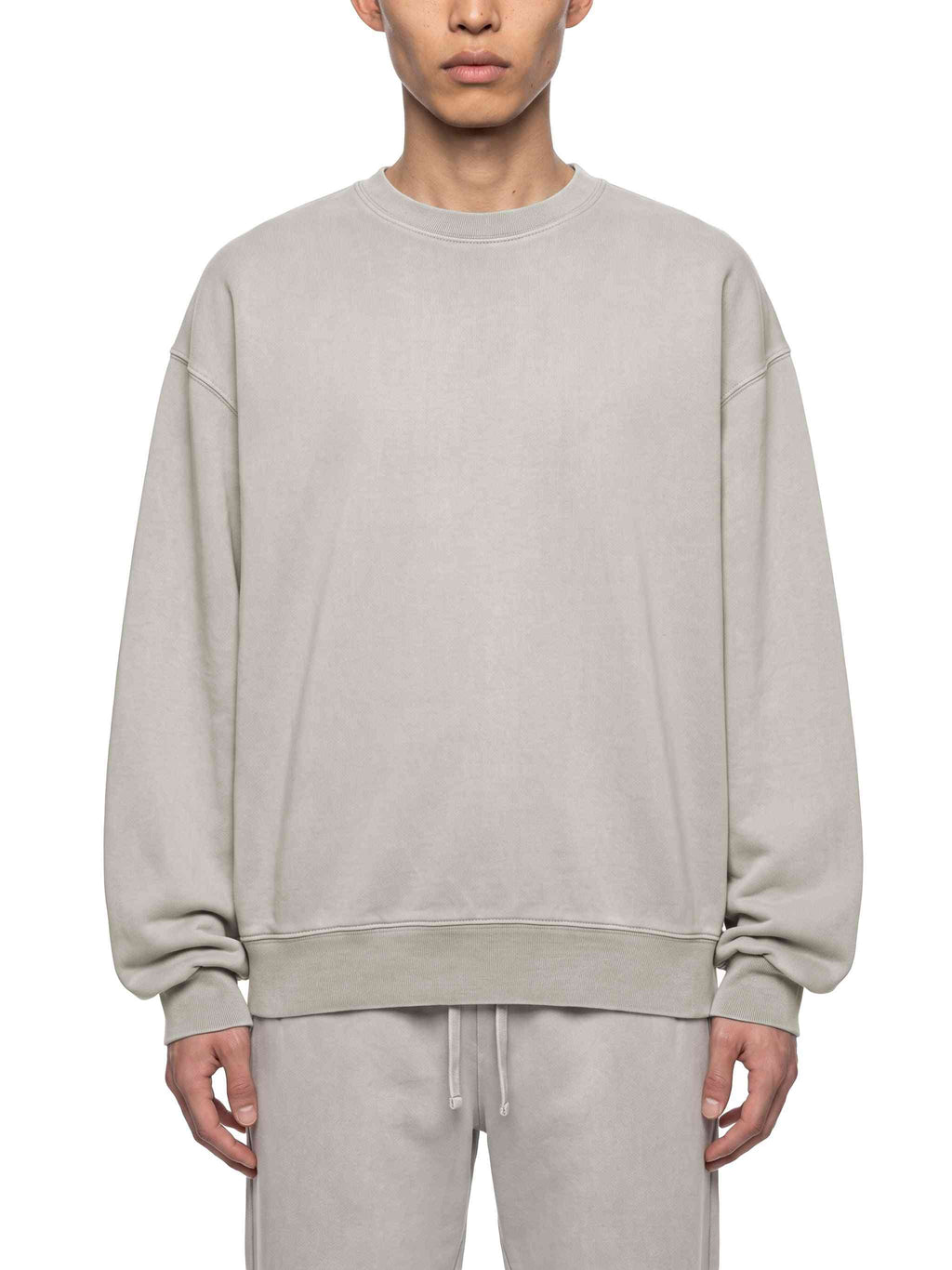 A model wearing a light gray crewneck sweatshirt and matching sweatpants against a plain white background.