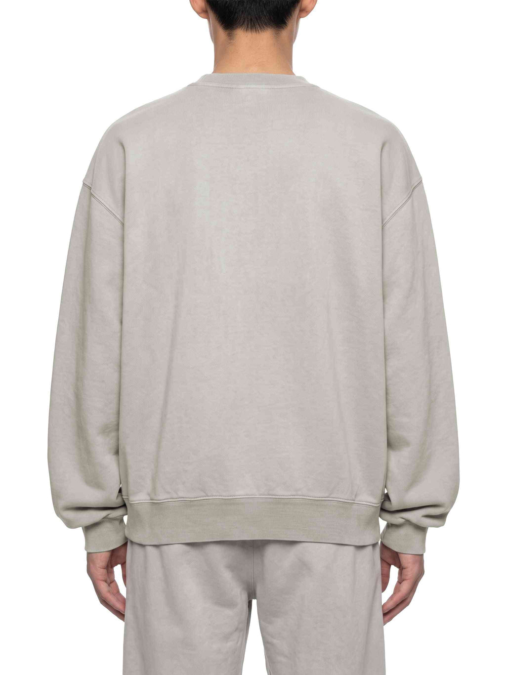 A person shown from the back wearing an oversized light beige crewneck sweatshirt and matching sweatpants against a plain white background.