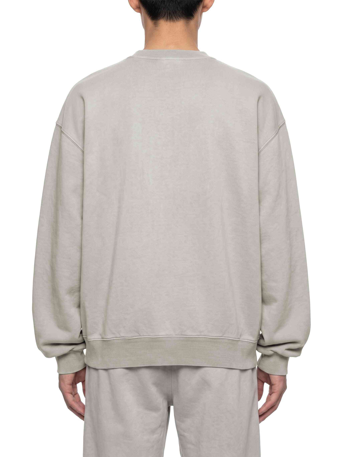A person shown from the back wearing an oversized light beige crewneck sweatshirt and matching sweatpants against a plain white background.