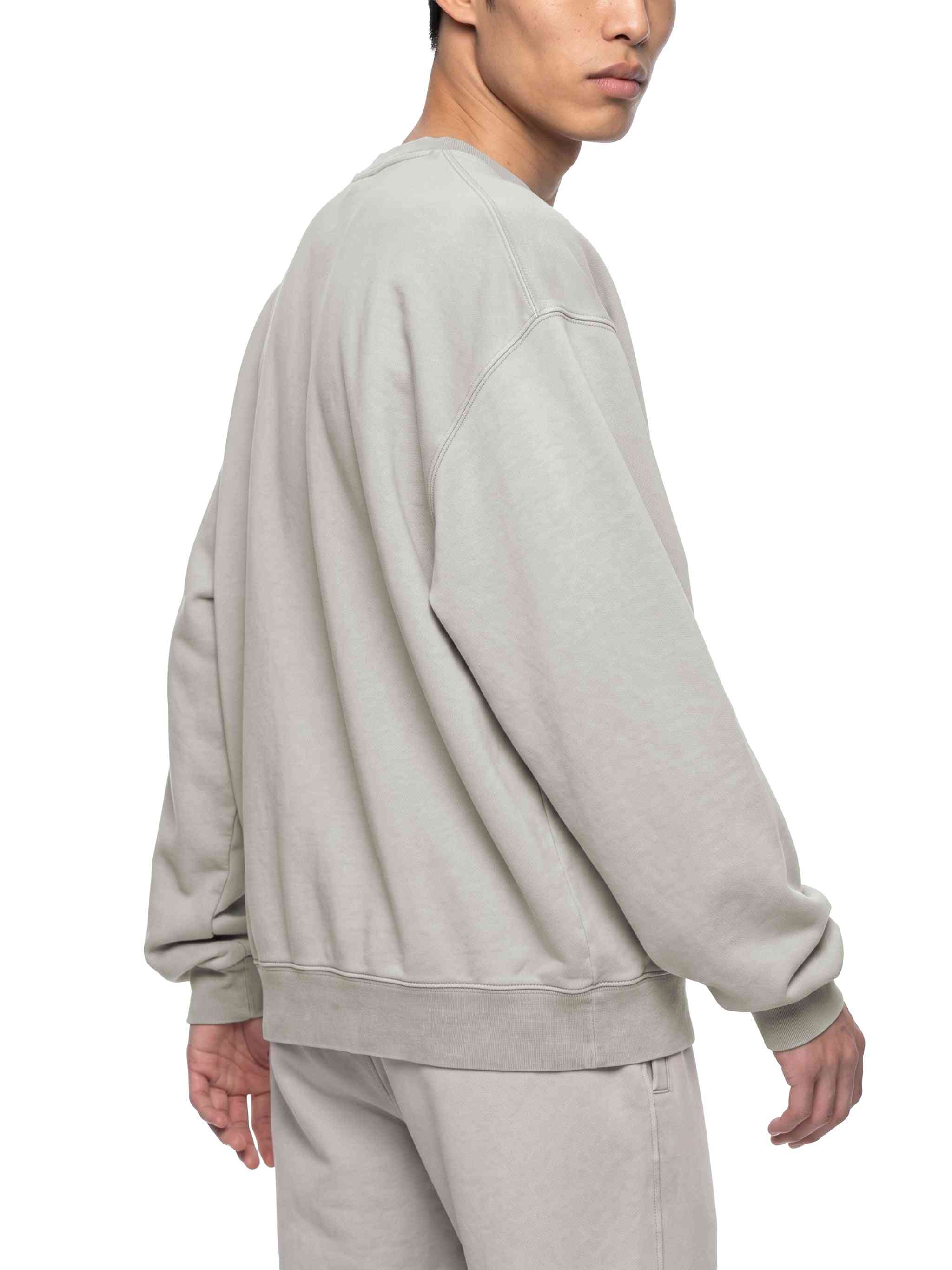 A man wearing an oversized light gray crewneck sweatshirt and matching sweatpants, shown from a side-back angle against a plain white background.