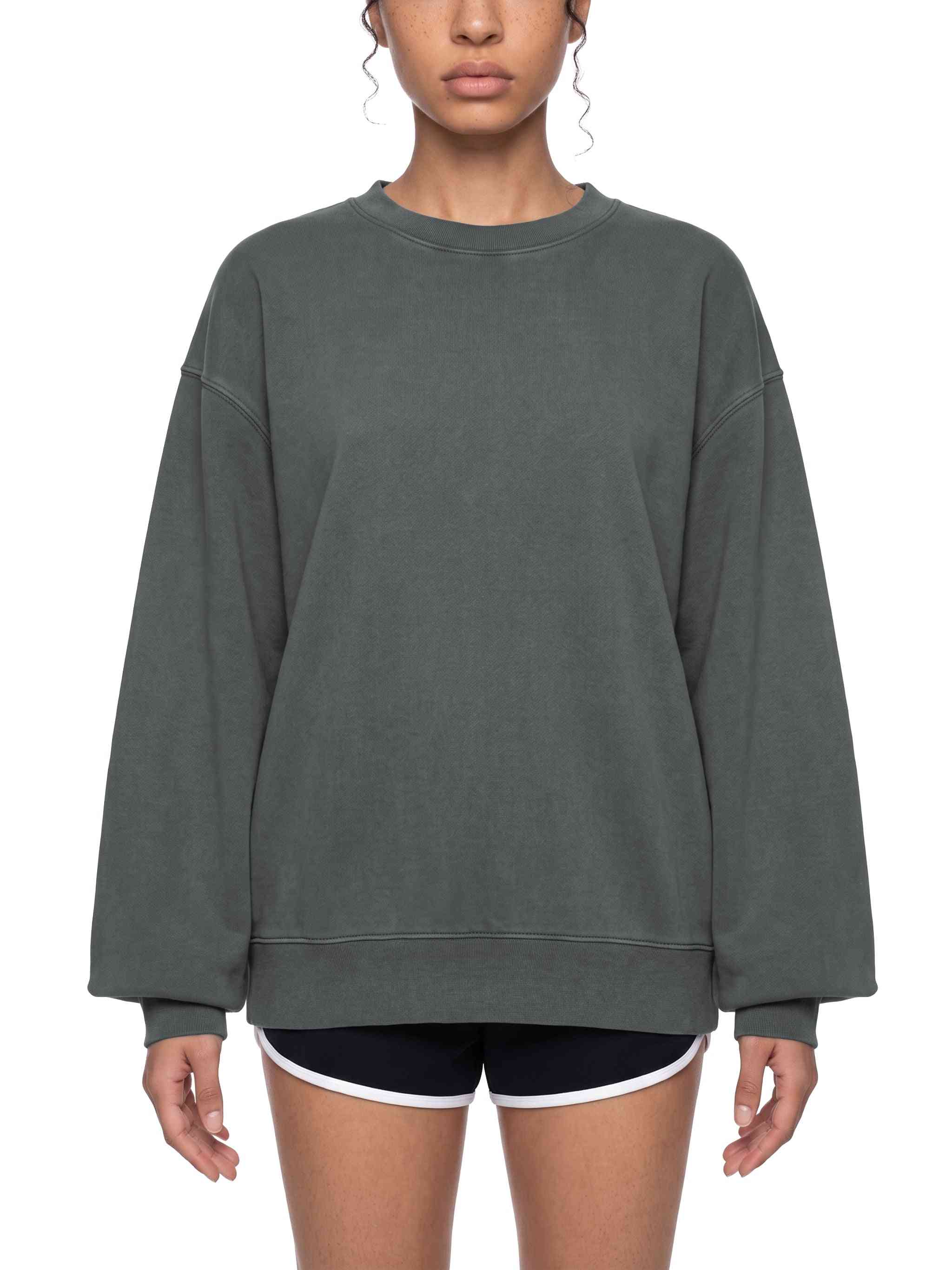 A woman wearing an oversized dark gray crewneck sweatshirt and black athletic shorts with a white trim, shown from the nose down against a plain white background.