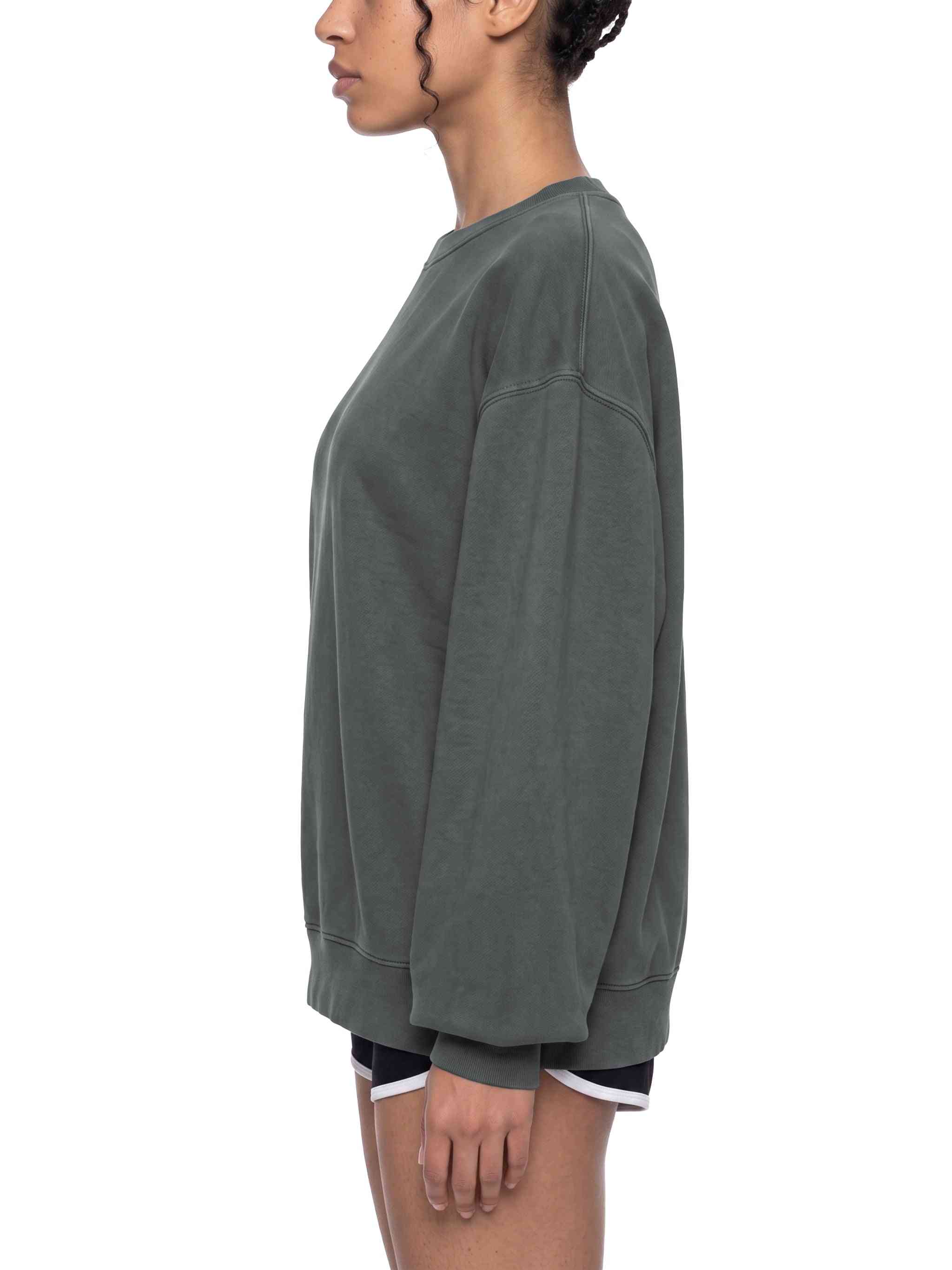A side-profile view of a model wearing an oversized, washed dark gray crewneck sweatshirt and black athletic shorts with a white trim, set against a plain white background.