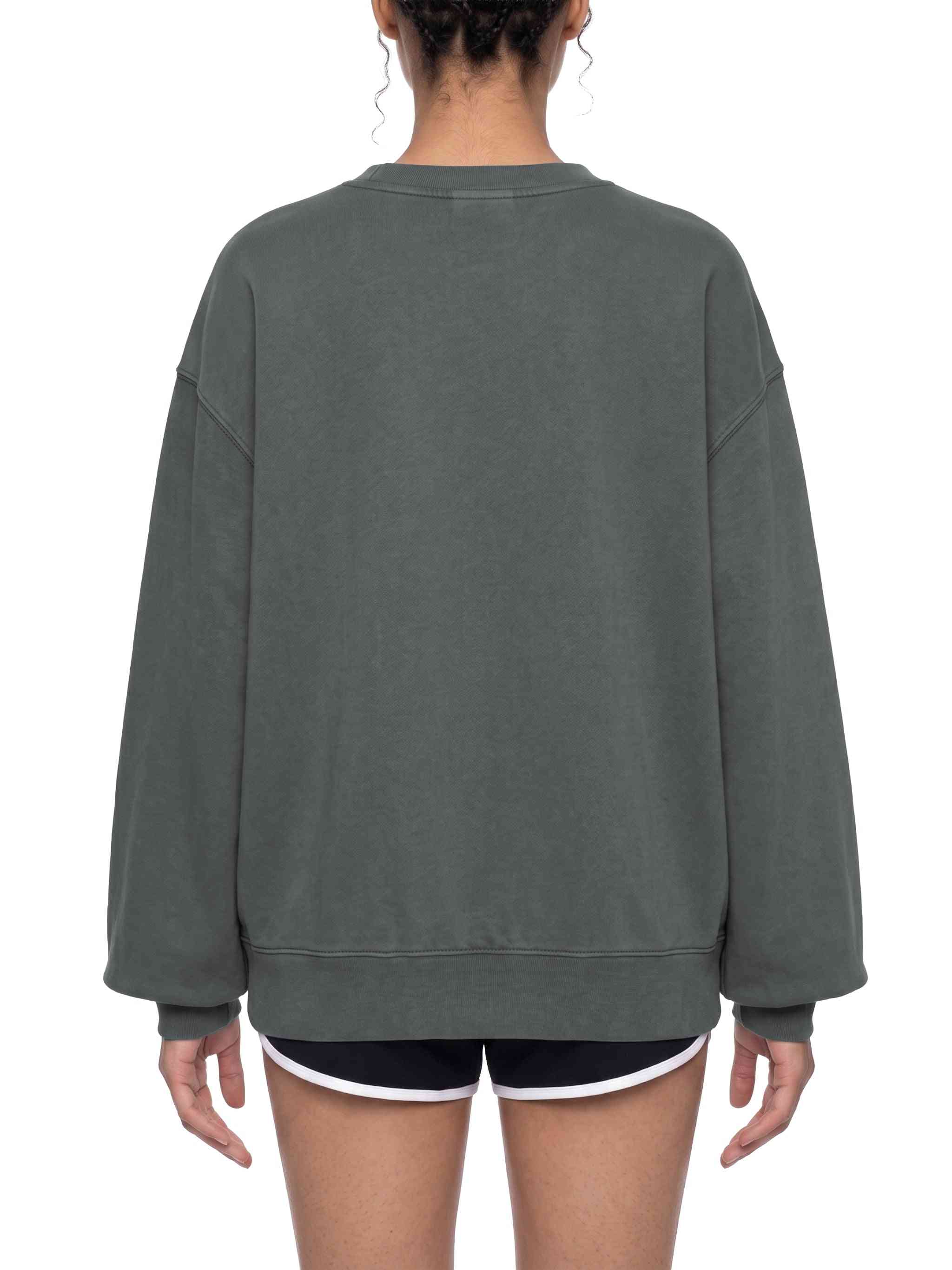 A person shown from the back wearing an oversized crewneck sweatshirt in a washed dark gray-green color, paired with black and white athletic shorts, against a plain white background.