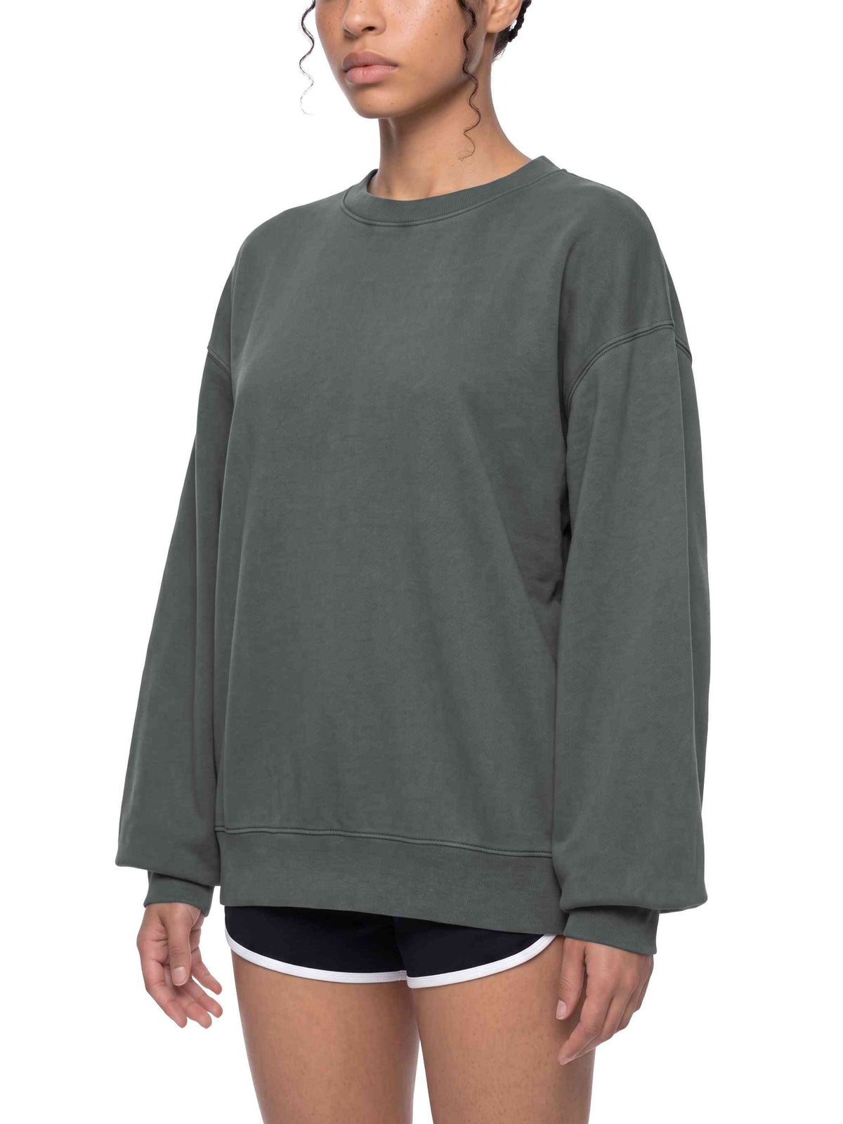 A woman wearing an oversized dark gray crewneck sweatshirt, paired with black athletic shorts that have a white trim, against a plain white background.